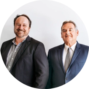 Two men standing side by side, both wearing suits and smiling, emanate a sense of camaraderie against a plain white background—a snapshot of professional mentoring.