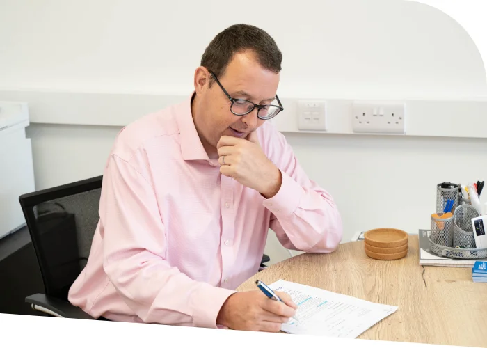 Martin Robertson is seated at a desk, writing in a notebook about the latest training programme. Office supplies are on the desk beside him.